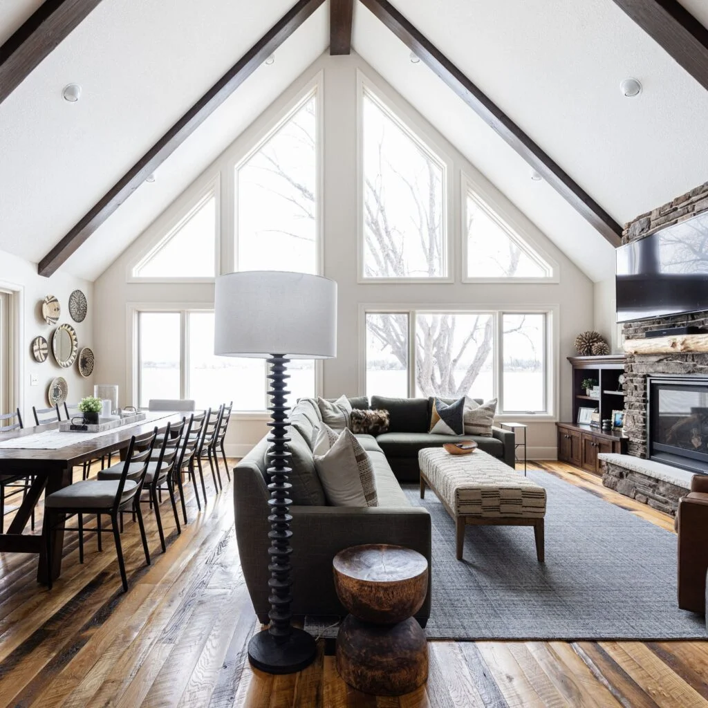 Image of a refined rustic A-frame cabin looking through an open concept living room to the large windows overlooking the lake